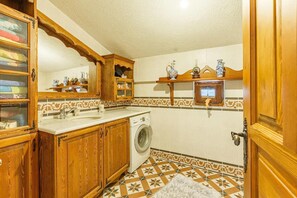 A compact kitchen with wooden cabinets, a washing machine, and a tiled backsplash.