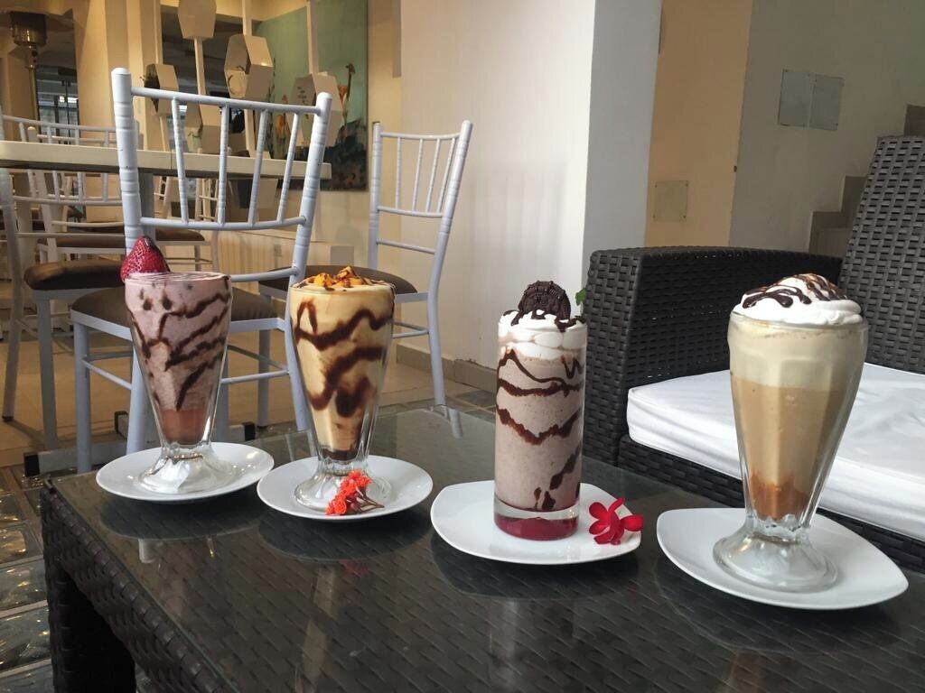 A table with four dessert drinks, a chair, and a wicker chair in a dining area.