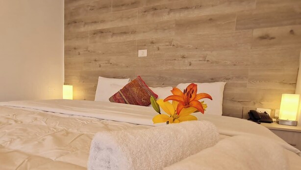 A hotel room with a wooden headboard, white bedding, a floral arrangement, and bedside lamps. - Tours Machu Picchu Perù Hotel (Cusco)