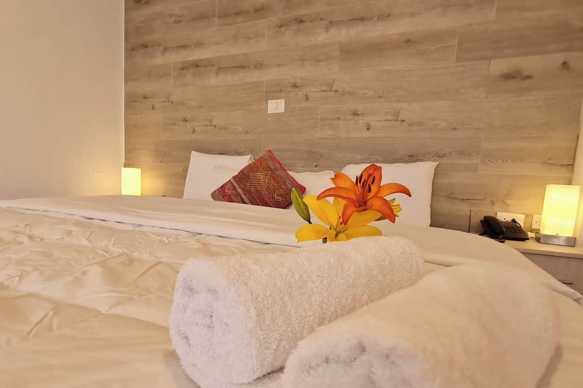A hotel room with a wooden headboard, white bedding, a floral arrangement, and bedside lamps.