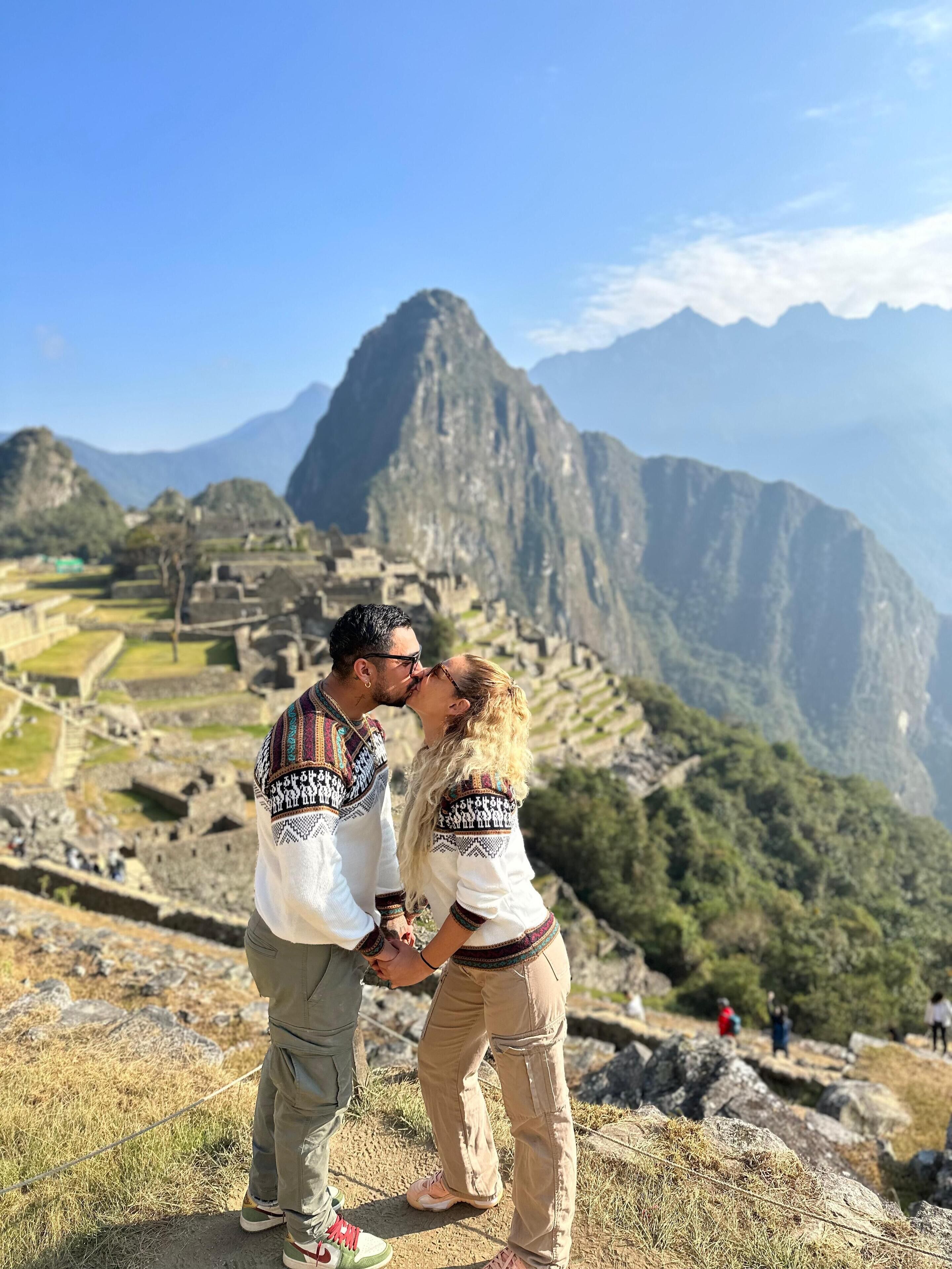 A couple kissing in front of Machu Picchu with the mountain range in the background.