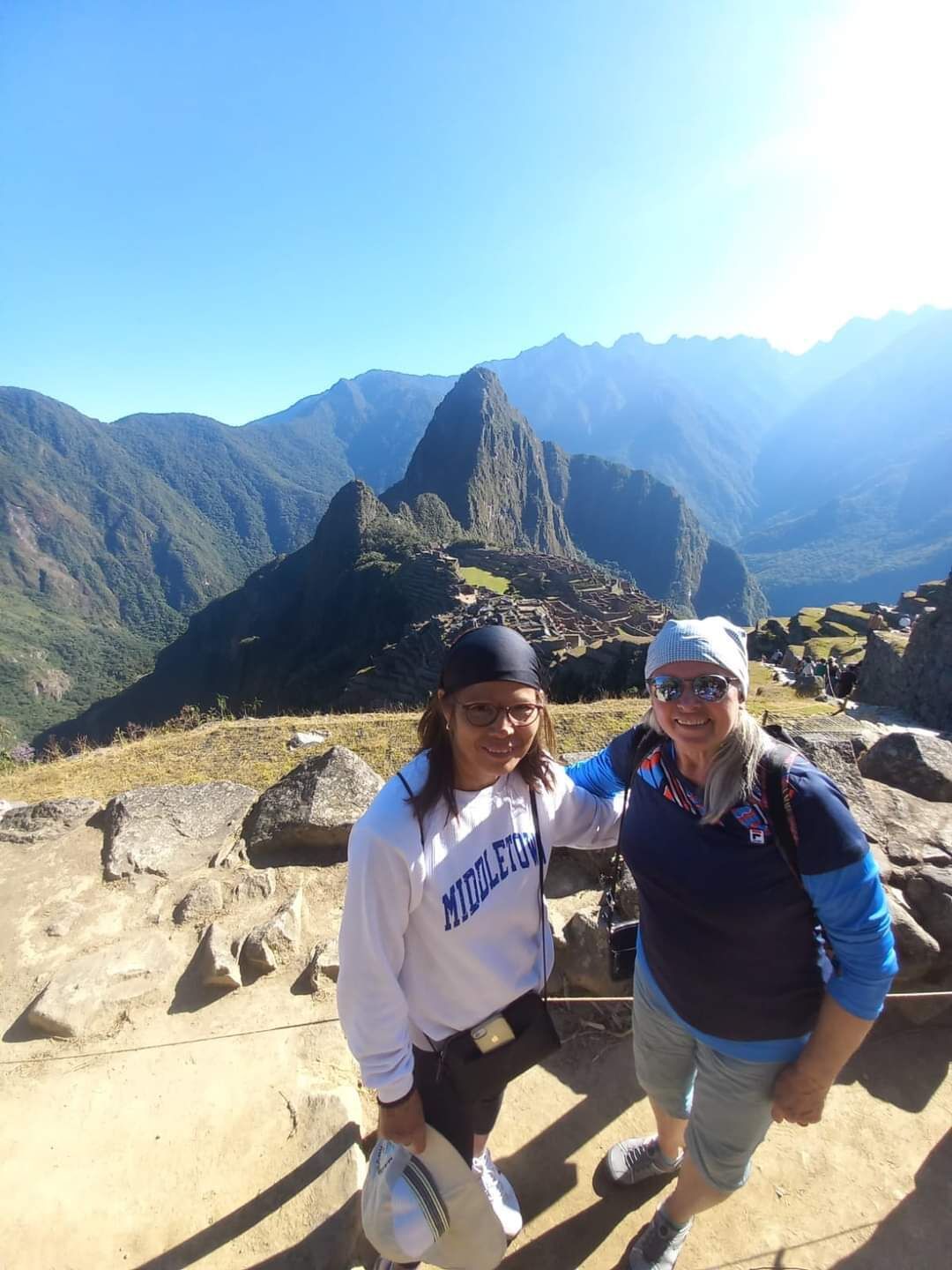 Two people standing on a rocky terrain with a mountainous landscape in the background.