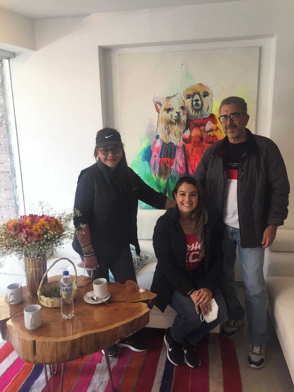 A room with a wooden table, a vase with flowers, and a painting of llamas on the wall.