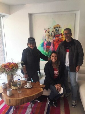 A room with a wooden table, a vase with flowers, and a painting of llamas on the wall. - Tours Machu Picchu Perù Hotel (Cusco)
