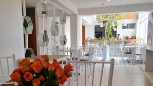 A dining area with a table set for two, a vase of orange flowers, and a view into the kitchen and dining space. - Tours Machu Picchu Perù Hotel (Cusco)