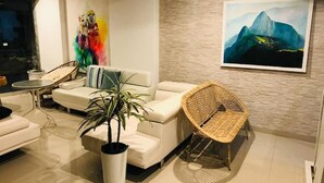 A modern living room with a white sofa, a wicker chair, a potted plant, and two paintings on the wall. - Tours Machu Picchu Perù Hotel (Cusco)