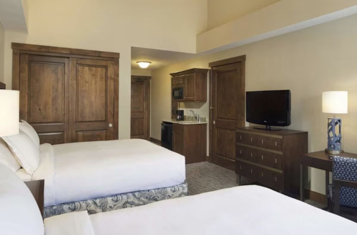 A hotel room with two beds, a television, a desk with a lamp, and wooden cabinets.