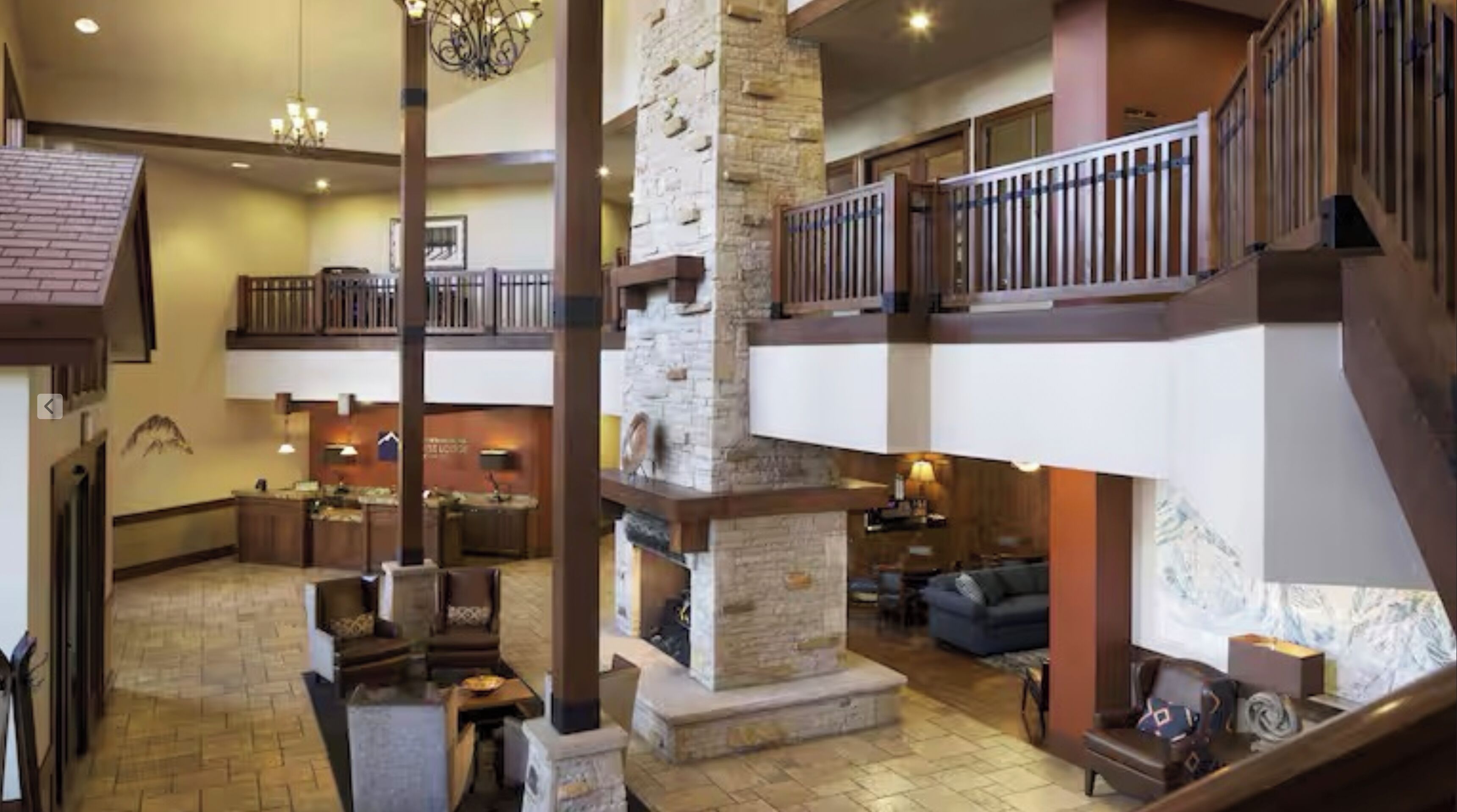 A spacious lobby with a stone fireplace, multiple seating areas, and a balcony with a railing.