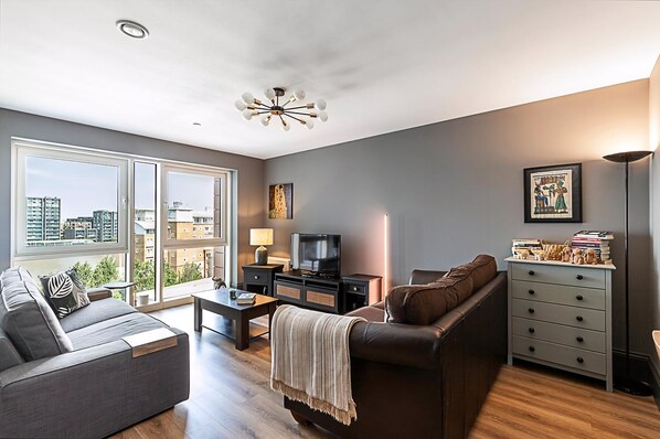 A modern living room with a sofa, a coffee table, a TV, and a lamp. - Riverside Escape With Breathtaking Thames Views (London)