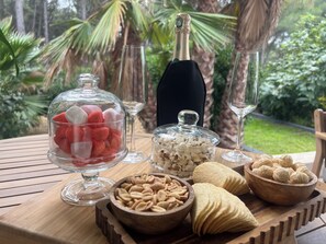 Une table dressée à l’extérieur, avec divers plats et une bouteille de champagne, et en toile de fond, une vue sur des palmiers.