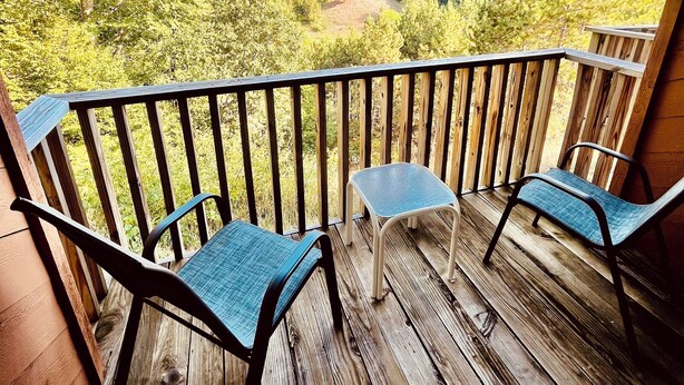 Un patio in legno con due sedie e un tavolino, con vista su un paesaggio boschivo.
