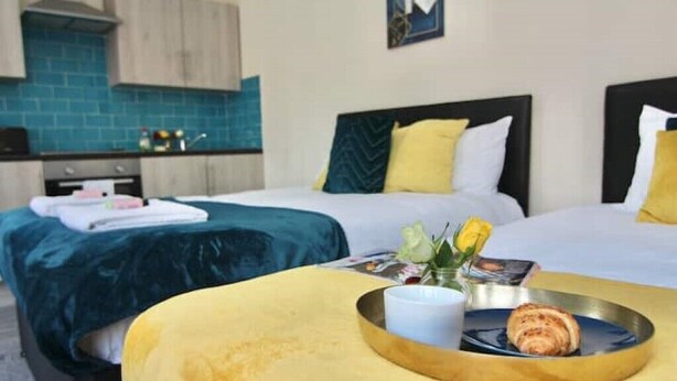 A hotel room with two beds, a kitchen area, and a breakfast tray with croissants. - LHR Studio 6 - Coventry (Coventry)