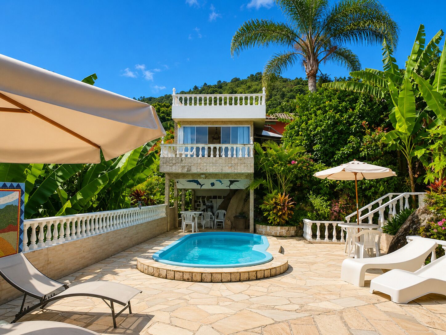 A two-story building with a swimming pool, outdoor seating, and lush greenery.