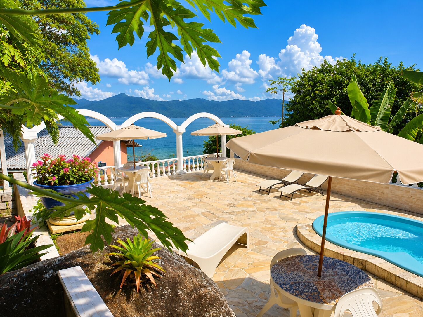 Zona junto a la piscina con vista al mar y montañas, mobiliario exterior y una pileta.