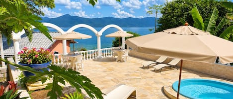 Zona junto a la piscina con vista al mar y montañas, mobiliario exterior y una pileta.
