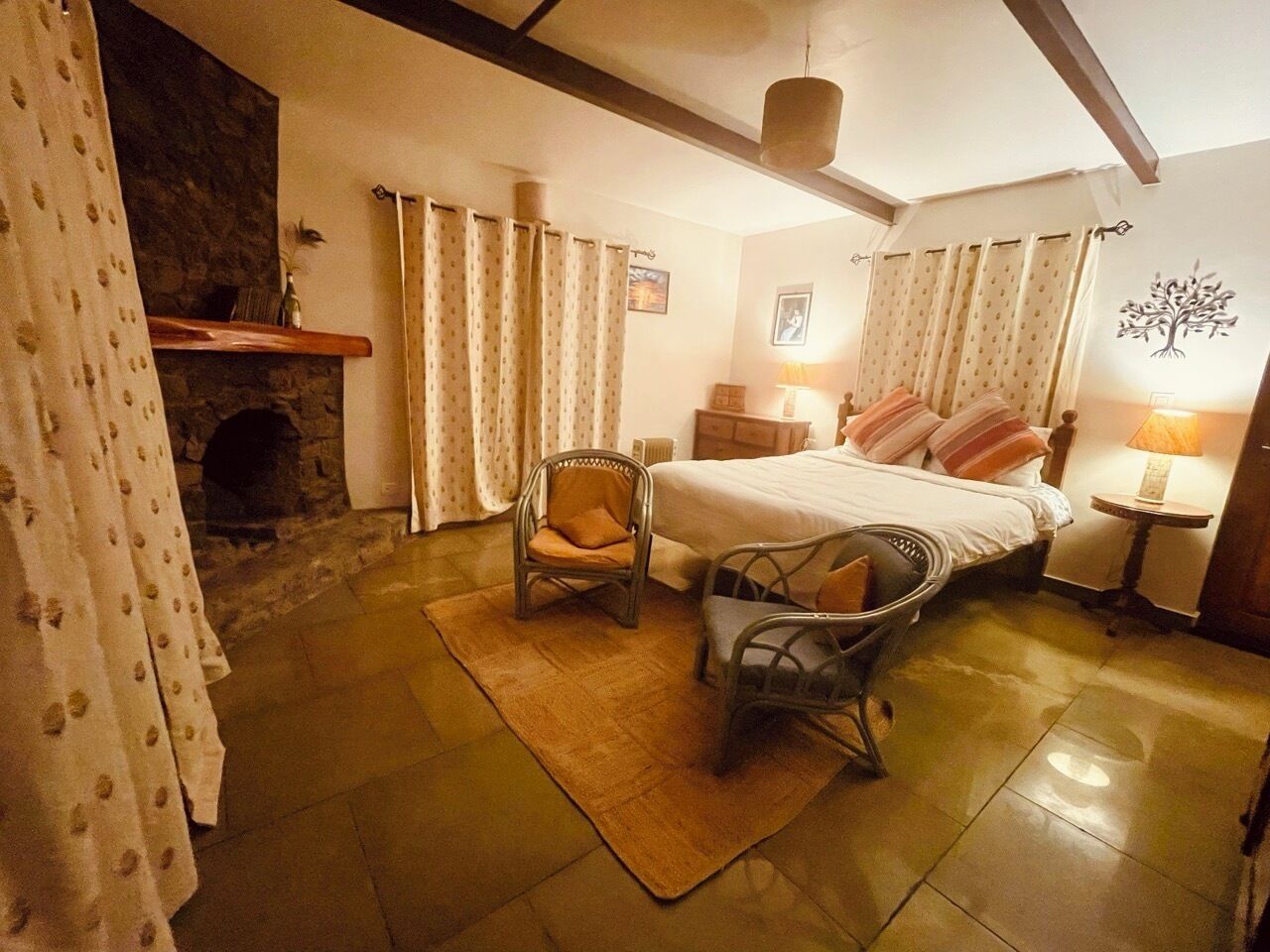 Um quarto aconchegante com uma cama, duas cadeiras, uma lareira e uma parede com um mural de árvore.