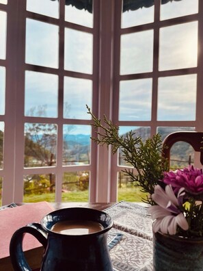 A view through a window with a clear sky, a table with a coffee mug, and a vase with flowers.