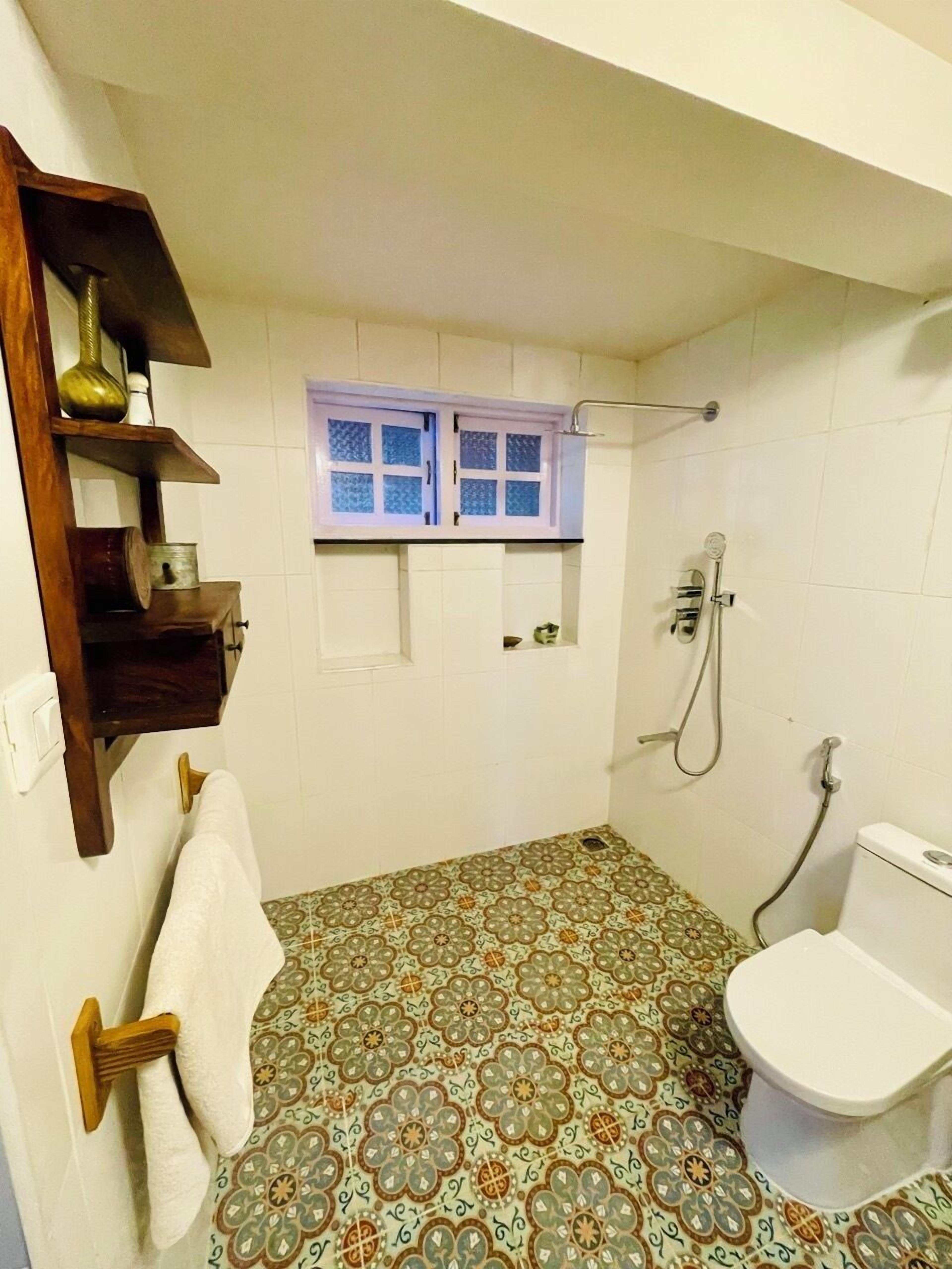 Un baño con baldosas de diseño en el suelo, un inodoro, una ducha y una ventana con vidrio esmerilado.