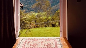 A room with a view of a green valley and hills through an open door. - Stumpfields (Ootacamund)