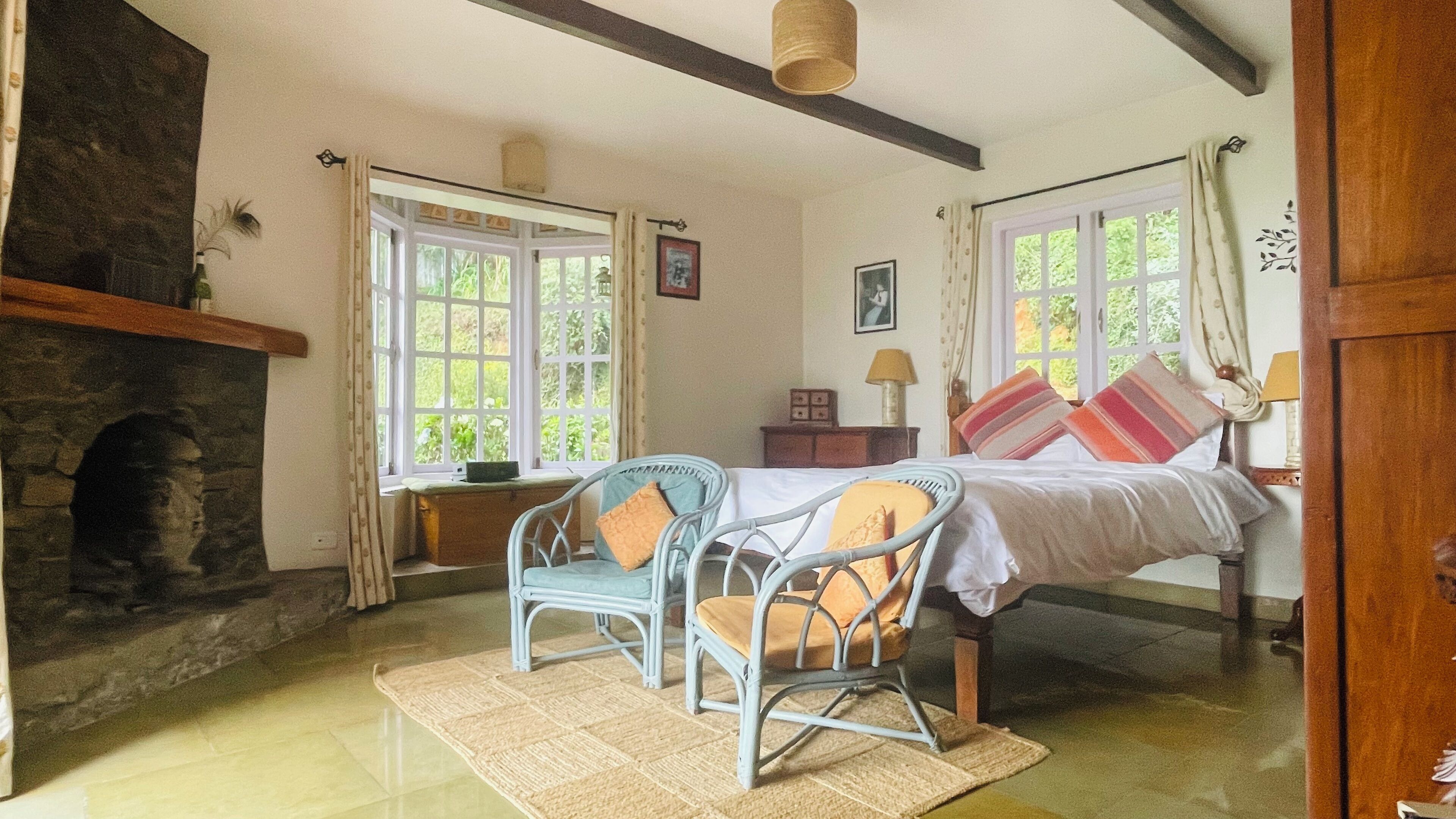 Un dormitorio con cama, dos sillones, chimenea y ventanas amplias.