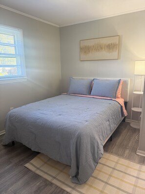 A bedroom with a bed, a window with blinds, a wall-mounted artwork, and a bedside lamp. - Cozy 1-bedroom condo in Burlington, pet friendly  (Burlington)