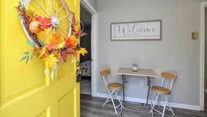 Une pièce avec une porte jaune, une pancarte de bienvenue et une petite table avec deux chaises.