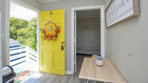 Une porte jaune vif, ornée d’une guirlande décorative, avec une pancarte indiquant « Bienvenue » et une petite table sur laquelle est posée une tasse.