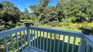 Une terrasse en bois, agrémentée de balustrades blanches, offre une vue sur une pelouse bien entretenue et une forêt dense.
