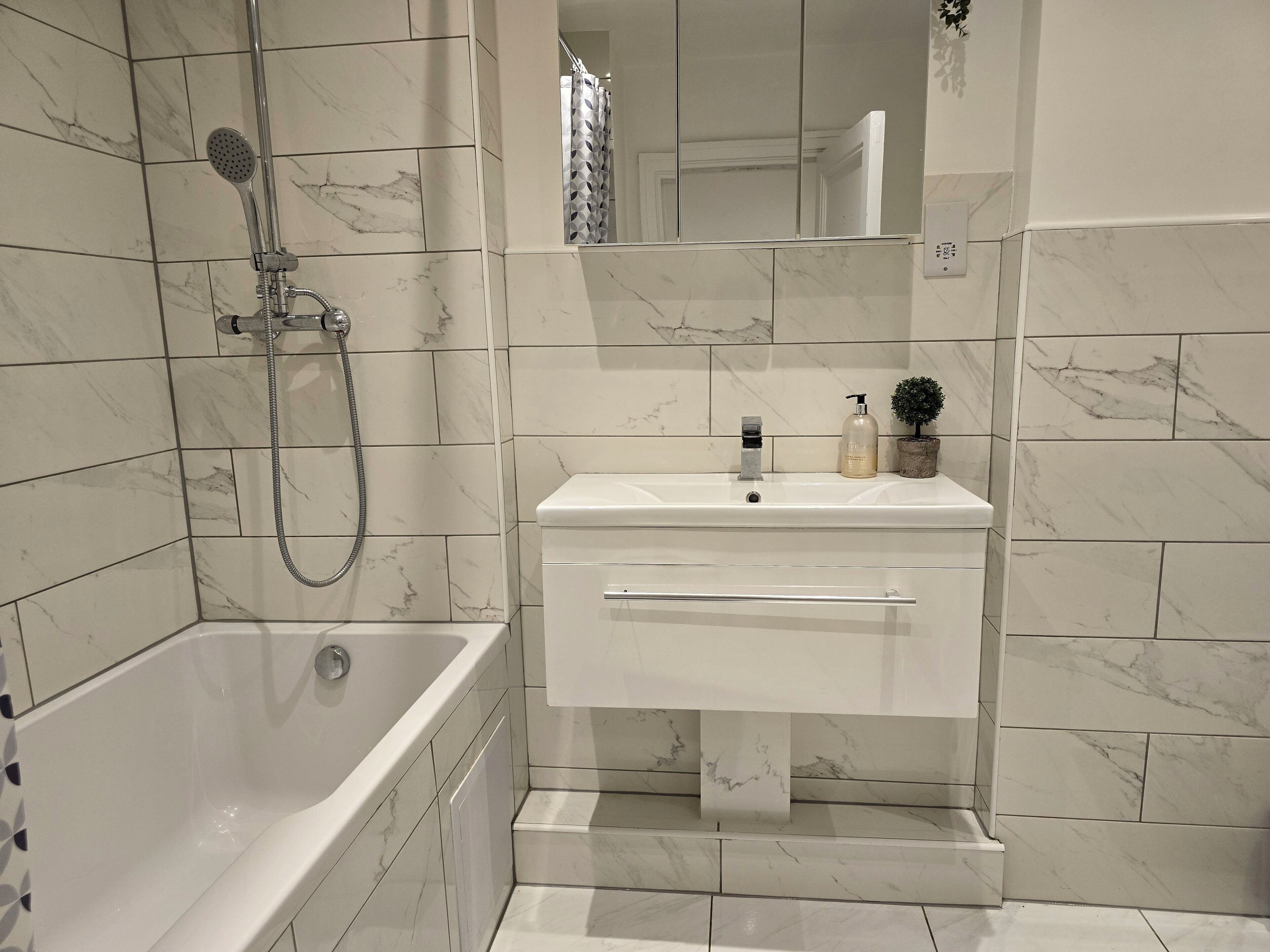 A bathroom with a bathtub, a sink with a mirror, and a showerhead.
