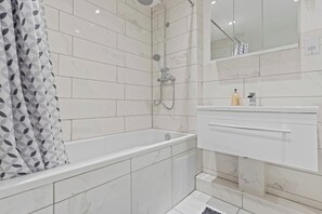 A modern bathroom with a bathtub, shower, and vanity. - Cozy Apt Step Away Hyde Park and Oxford Street (London)
