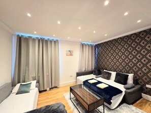 A modern living room with a sofa, a smaller couch, a glass coffee table, and a patterned wall. - Cozy Apt Step Away Hyde Park and Oxford Street (London)