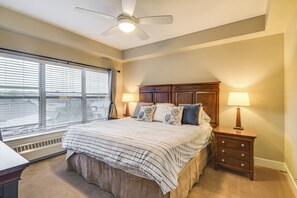 Een slaapkamer met een groot bed, twee bedlampen, een plafondventilator en uitzicht door grote ramen.