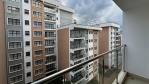 Un immeuble résidentiel à plusieurs étages, doté de balcons et d’une rambarde en verre, avec un ciel nuageux en arrière-plan.