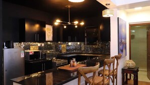 Une cuisine moderne avec des meubles de couleur noire, un plan de travail noir et un îlot central. Deux luminaires suspendus sont placés au-dessus de l’îlot, et un four à micro-ondes se trouve sur le plan de travail.