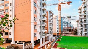 Un immeuble résidentiel à plusieurs étages, doté de balcons, avec une grue de construction et une pelouse verdoyante.