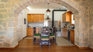 Una cocina con paredes de piedra, armarios de madera, una mesa de comedor con sillas y una lámpara colgante.