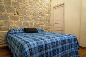 A bed with a plaid bedspread, a stone wall, and a wooden door.
