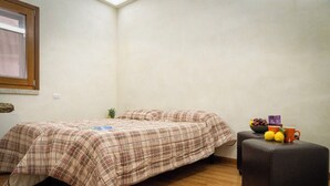 Un dormitorio con cama, una mesita con frutas y una caja, y una planta en maceta.