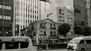 Vista de la calle con un edificio de arquitectura tradicional, un letrero y una furgoneta estacionada.