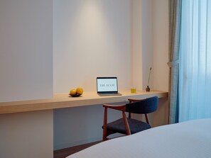 Habitación de hotel moderna con un escritorio de madera, una computadora portátil, dos naranjas, un vaso de bebida amarilla y una silla.