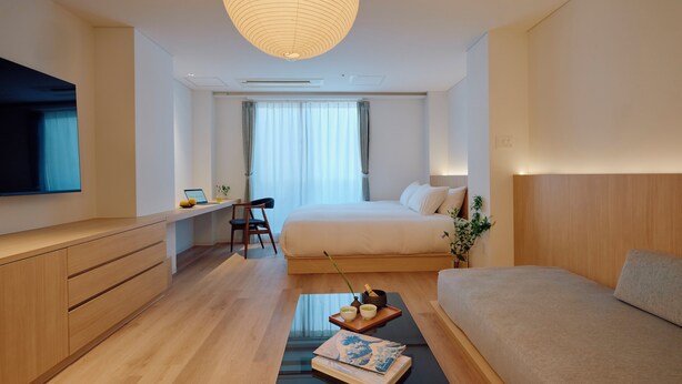Una habitación de hotel moderna con una cama, un escritorio, una silla, un televisor y un ventanal grande.