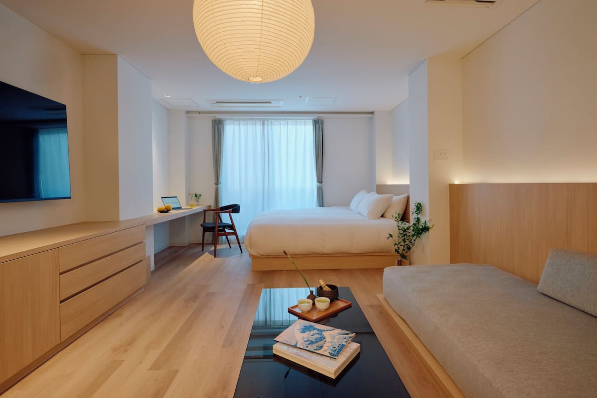 A modern hotel room with a bed, a desk, a chair, a TV, and a large window.