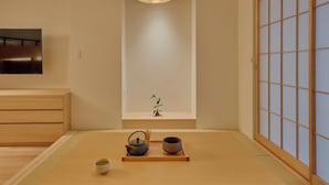 Una habitación japonesa tradicional con suelo de tatami, una mesa baja con un juego de té, una planta pequeña y puertas correderas.
