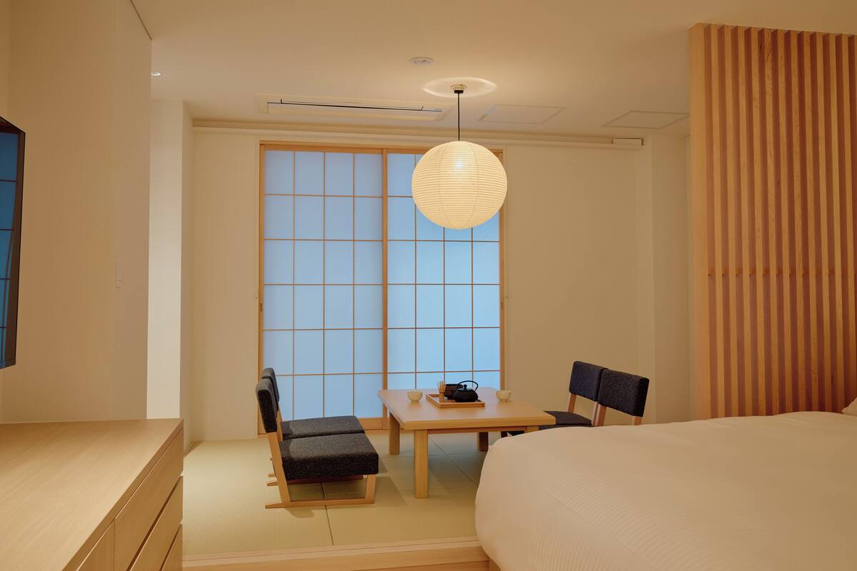 A traditional Japanese-style room with tatami flooring, a low table with a tea set, a sofa, and a bed.