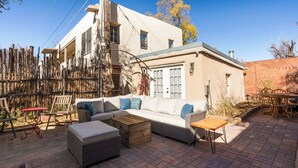 Eine Terrasse mit einer Couch, einem Hocker und einem Tisch, umgeben von einem Holzzaun und einer Ziegelmauer.