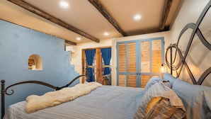 Ein Schlafzimmer mit einem Bett, Holzbalken, einem kleinen Fenster und einer Tür mit blauen Vorhängen.