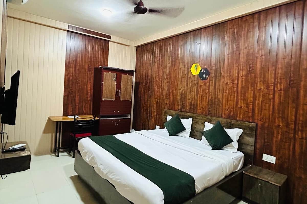 Une chambre à coucher avec une tête de lit en bois, un lit avec une literie blanche et verte, un bureau avec une chaise et un téléviseur.