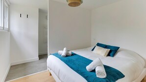 A modern bedroom with a large bed, teal and white bedding, a hanging light fixture, and a view of a hallway. - Lancelot - appt 4 pers (Bruz)