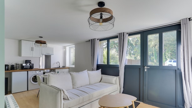 A modern kitchen with a built-in washing machine, a sofa, and a dining area with a table and chairs. - Lancelot - appt 4 pers (Bruz)
