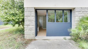 A modern building entrance with a stone facade, a blue door, and a pathway leading to a hallway. - Lancelot - appt 4 pers (Bruz)